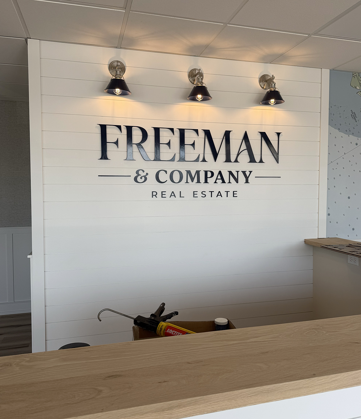 Custom dimensional Freeman & Company Real Estate lobby logo installed on a white shiplap feature wall with accent lighting on Long Beach Island, New Jersey