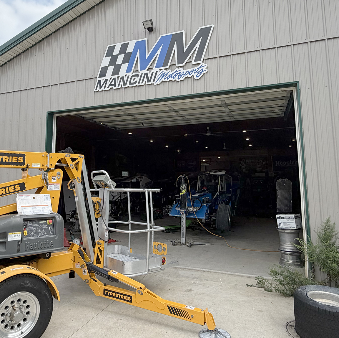 Custom three-dimensional Mancini Motorsports race shop wall sign installed above the garage entrance in New Gretna, New Jersey using aerial lift equipment